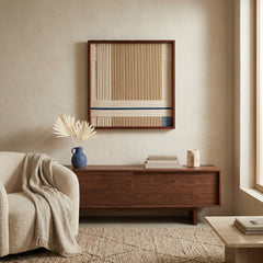 Modern hand-woven wool wall hanging styled above a mid-century modern wooden credenza with neutral decor and a blue ceramic vase.