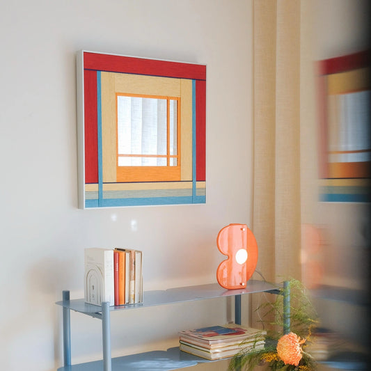 Angled view of the colorful hand-woven wool mirror on a white wall, reflecting light and adding a playful touch to the room.