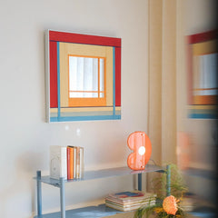 Angled view of the colorful hand-woven wool mirror on a white wall, reflecting light and adding a playful touch to the room.
