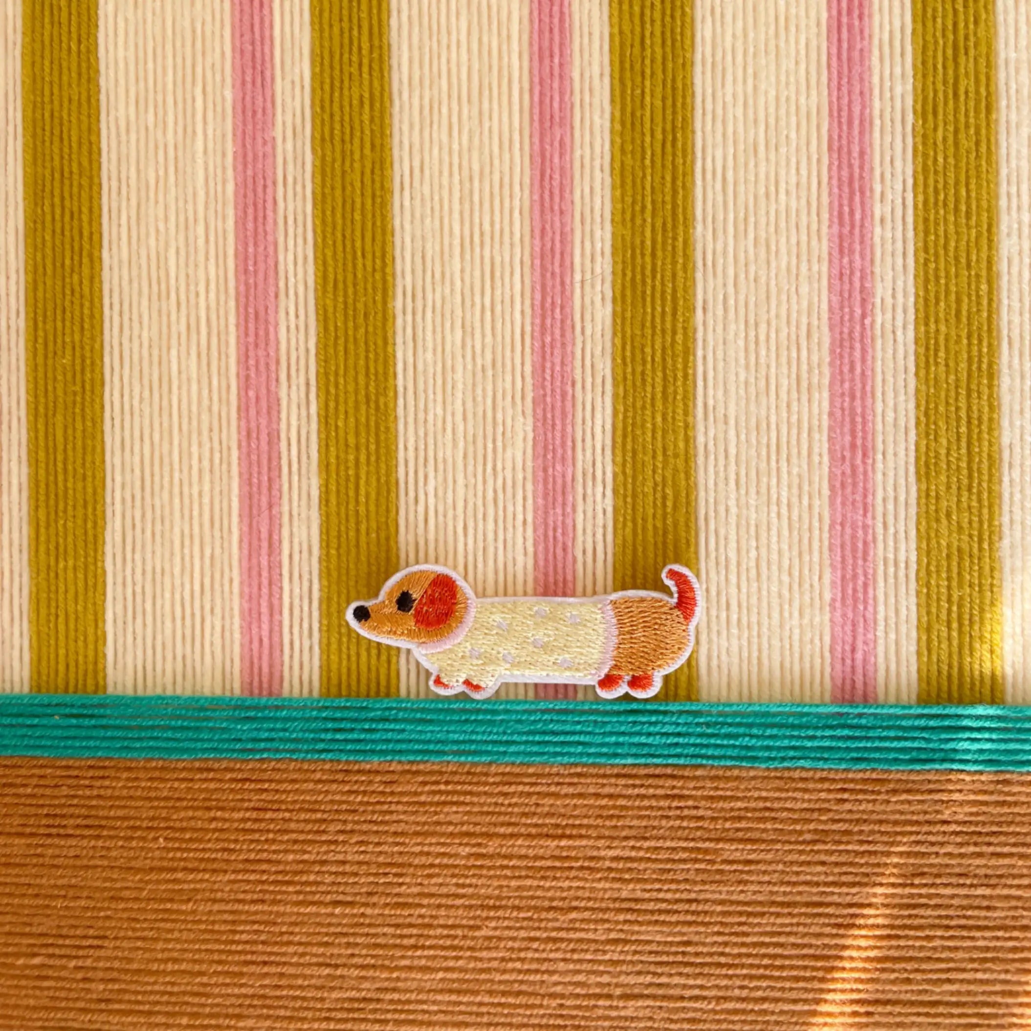 Macro shot of the hand-woven wool texture showing the raised coral and olive stripes and the embroidered dog character detail.