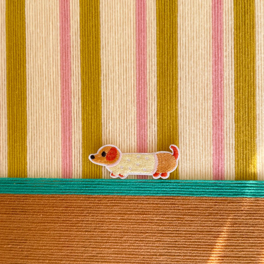 Macro shot of the hand-woven wool texture showing the raised coral and olive stripes and the embroidered dog character detail.