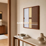 Diluted Solitude gray yellow and brown textile wall art shown from an angled view above a slim console in a minimalist entryway.