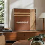 Earth’s Embrace chocolate brown and sand cream geometric yarn wall art styled on a wood cabinet beside books and a pleated lamp.