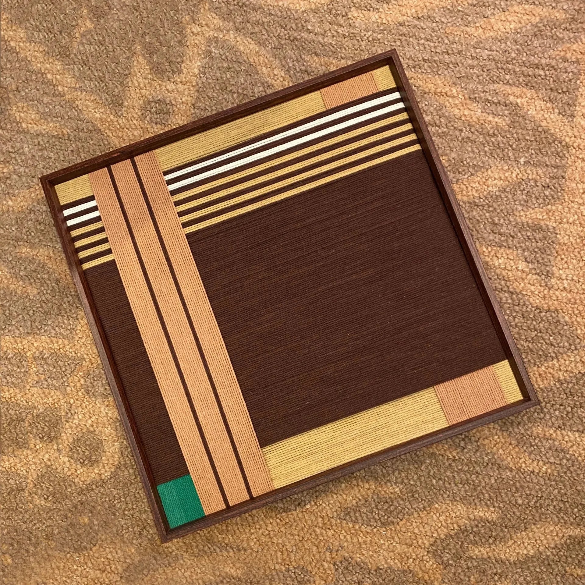 Overhead flat lay of Earthy Fragrance yarn wall art showing its uniform earth-tone stripe widths and precise square proportions
