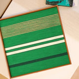 Endless Flow soft cotton cord fiber wall art with green stripe pattern displayed on a desk alongside yarn balls and a lamp, highlighting its square format and vibrant texture
