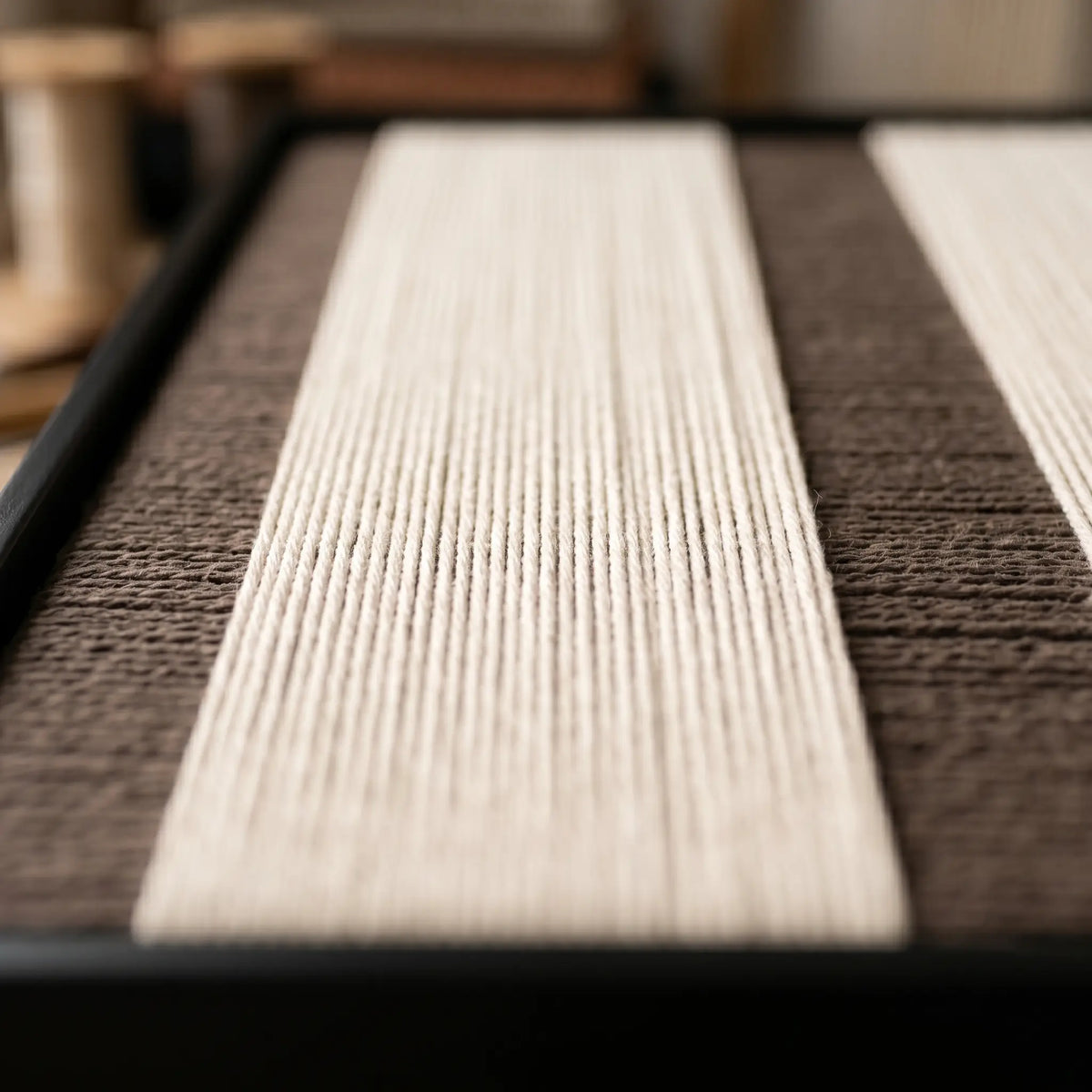 Angled close-up of the framed Eternal Colonnade hand-woven tapestry, showing the wooden frame depth and the precision of the cream and brown weave.
