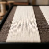 Angled close-up of the framed Eternal Colonnade hand-woven tapestry, showing the wooden frame depth and the precision of the cream and brown weave.
