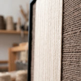 Extreme macro close-up of the Eternal Colonnade hand-woven textile art, highlighting the dimensional cream and dark brown yarn textures within the black frame.