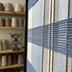 Extreme angled macro close-up of the Foggy Pier hand-woven textile art highlighting the textured navy blue horizontal yarn crossing over light blue, grey, and cream vertical stripes.