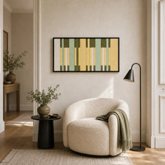 Framed hand-woven wool tapestry styled in a cozy reading nook, positioned above a small black table next to a white curved armchair.