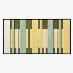 Frontal studio shot of the Garden Interval hand-woven wool wall art featuring green and yellow geometric patterns in a black frame.
