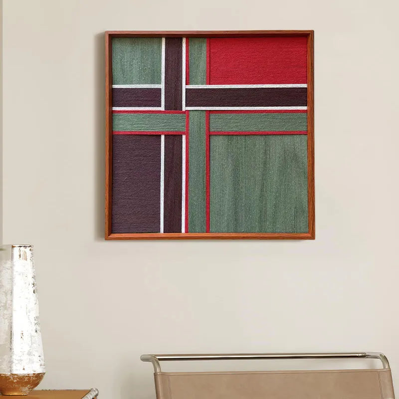 Front view of the hand-woven fiber art piece on a plain wall, highlighting the structured red and green color blocks and wooden frame.