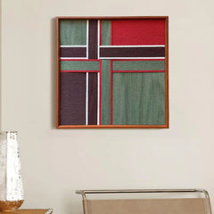 Front view of the hand-woven fiber art piece on a plain wall, highlighting the structured red and green color blocks and wooden frame.