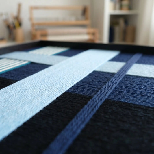 Detailed macro shot of Glacial Stationeries hand-woven wool art featuring interlocking navy, ice blue, and charcoal grey hand-wrapped yarn.