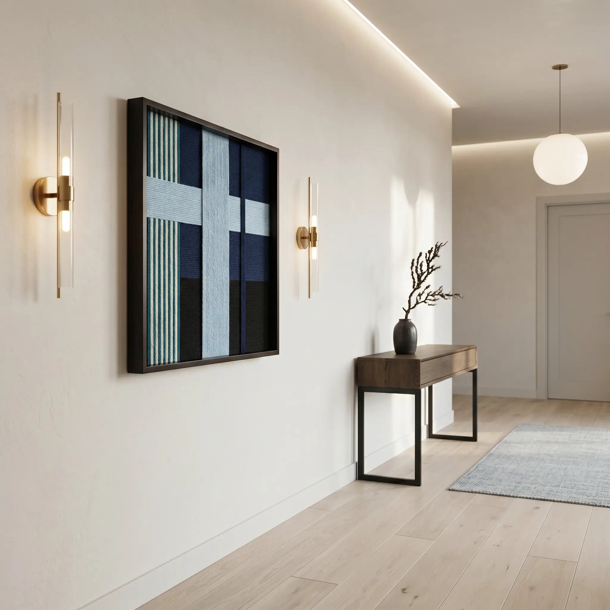 Square blue textured fiber art hanging in a minimalist hallway above a wood console table with gold wall sconces.