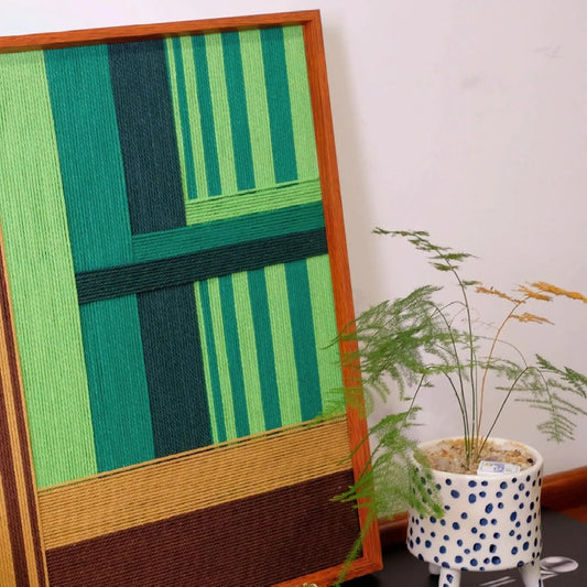 The Summer Mountain Walk fiber art piece displayed near a potted plant, emphasizing its nature-inspired color palette of emerald and forest greens.