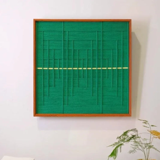 Green Shadow Weave hand-woven wool yarn wall art with dense vertical green stripes intersected by a pale-yellow horizontal line, framed in natural wood and displayed on a console table
