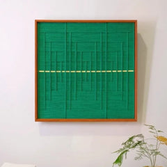 Green Shadow Weave hand-woven wool yarn wall art with dense vertical green stripes intersected by a pale-yellow horizontal line, framed in natural wood and displayed on a console table
