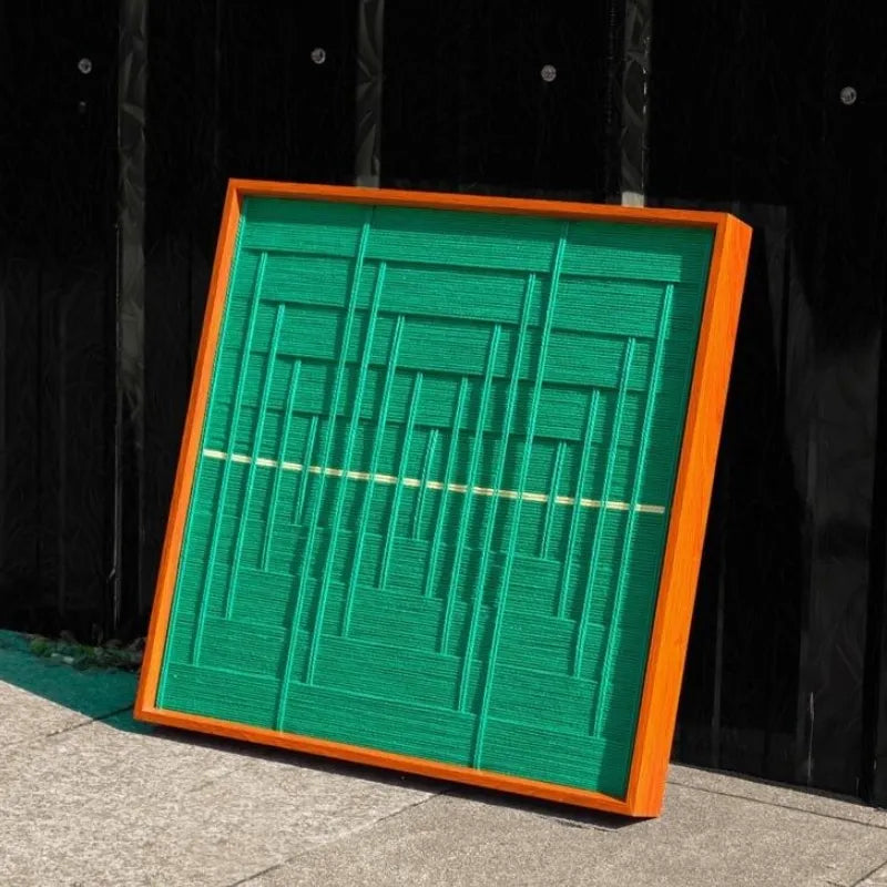 Hand-held view of Green Shadow Weave yarn wall art showing its precise square format, bold green stripe weave, and yellow accent line
