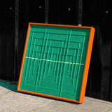 Hand-held view of Green Shadow Weave yarn wall art showing its precise square format, bold green stripe weave, and yellow accent line
