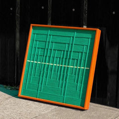 Hand-held view of Green Shadow Weave yarn wall art showing its precise square format, bold green stripe weave, and yellow accent line

