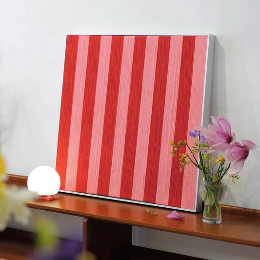 Angled view of Hana & Alice yarn woven art leaning on a tabletop beside a lamp and vase, showcasing the handcrafted texture and depth of the red stripe pattern
