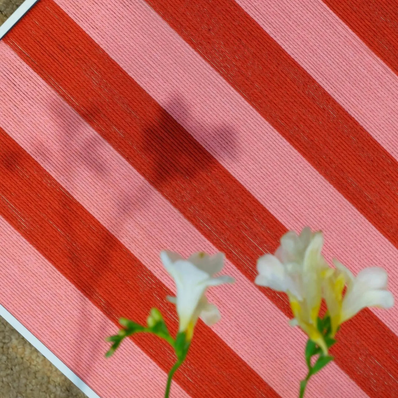 Macro shot of Hana & Alice yarn art framed by fresh blossoms, emphasizing the tactile stitch work and rich red hues
