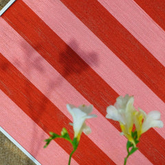 Macro shot of Hana & Alice yarn art framed by fresh blossoms, emphasizing the tactile stitch work and rich red hues
