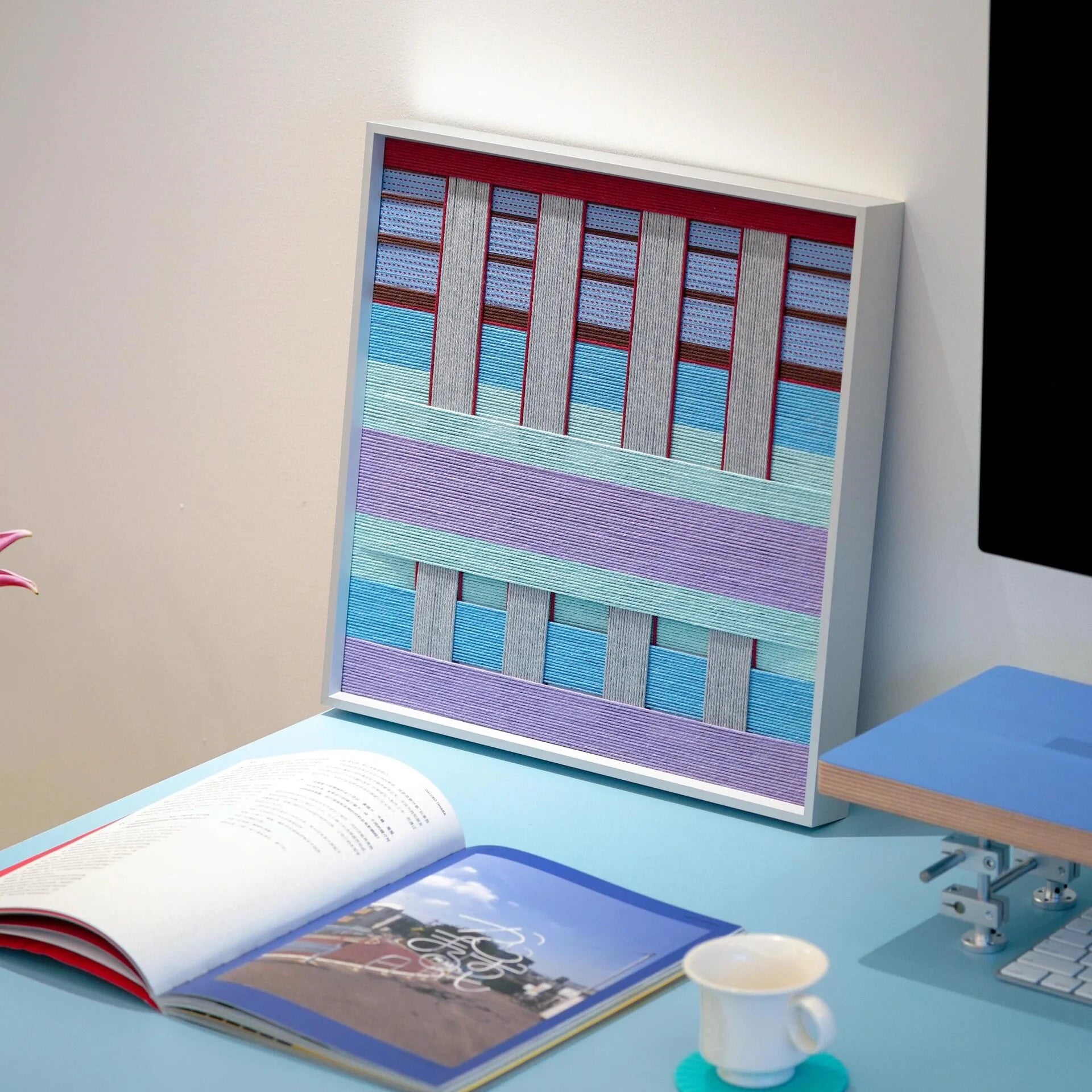 Close-up of Hanosen Anji yarn wall art revealing tight stitch detail and the interplay of pastel and red grid fibers
