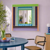 Hidden Forest green, purple, blue, and orange yarn-framed mirror displayed above a round blue table in a modern dining room.