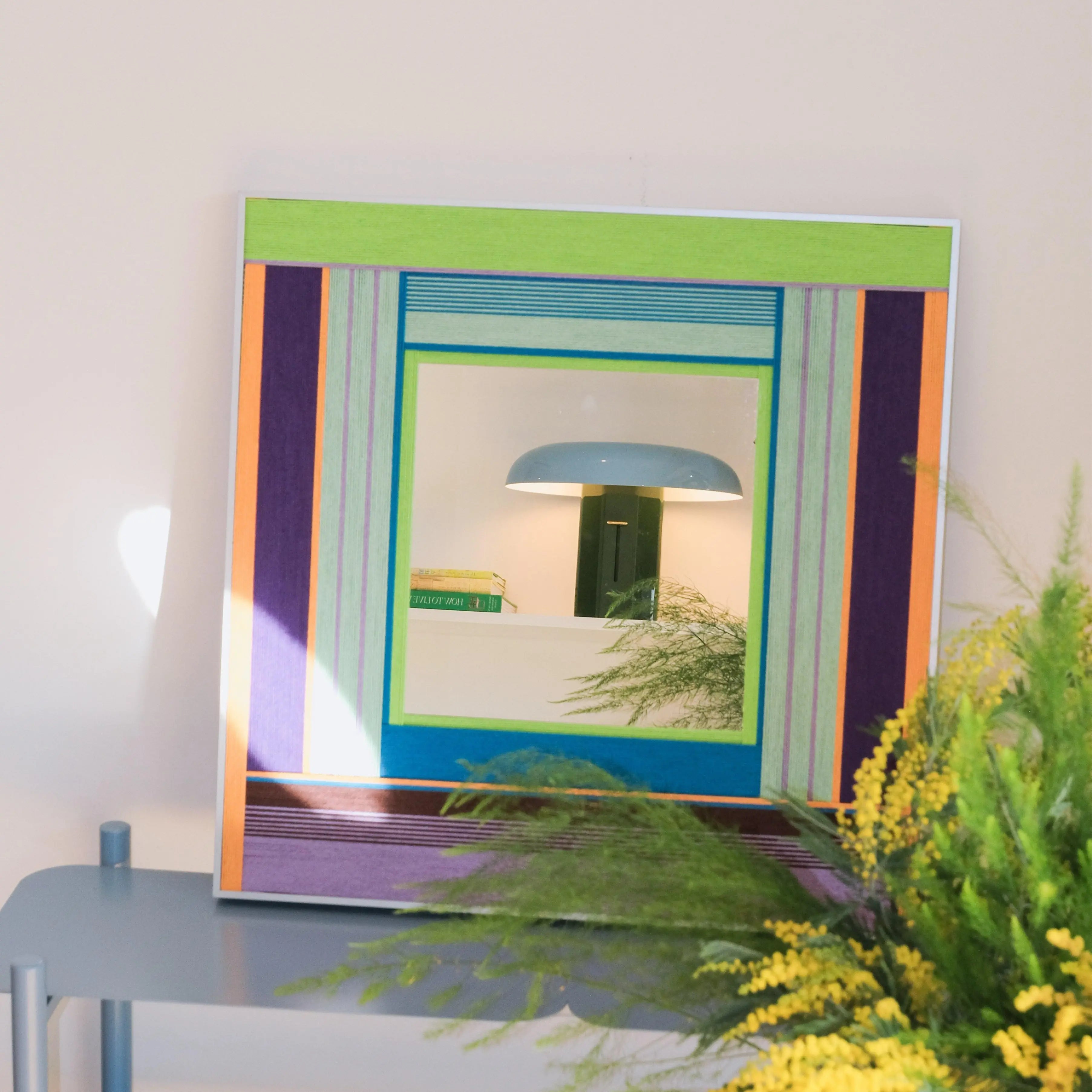 Hidden Forest yarn mirror art displayed on a shelf beside books and foliage, highlighting its compact square form and tranquil color palette.
