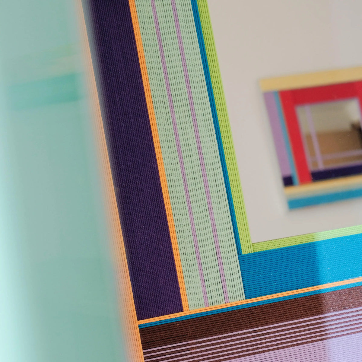 Close‑up of Hidden Forest yarn mirror art border revealing looped soft cotton cord texture and crisp transitions between green, purple, and wood hues.
