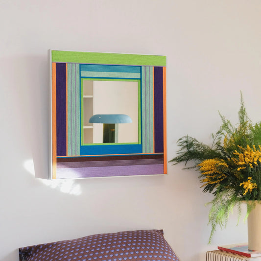 Hidden Forest mirror art mounted on a wall next to a potted plant, showcasing its deep green and purple stripe pattern around the reflective center.
