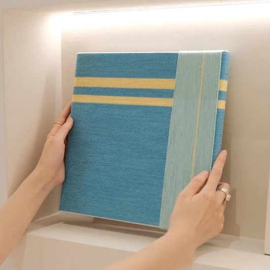 Hand-held view of Infinite Serenity yarn wall art showing its compact square form and crisp geometric stripe pattern of yellow accents and blue fields

