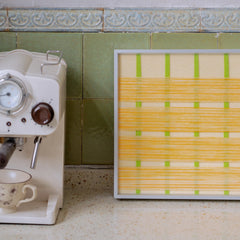 The yellow variation of the Spring Breeze art styled next to a coffee machine, showing how fiber art adds warmth and personality to kitchen spaces.