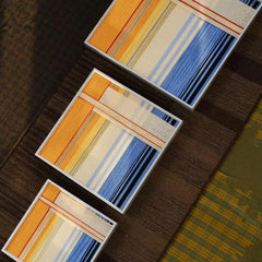 A collection of various sized framed wool tapestries with warm sunset hues arranged on a dark wooden surface to show scale.