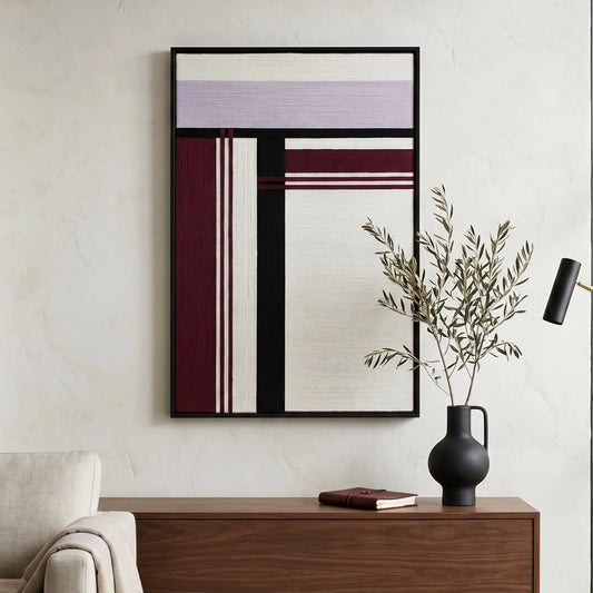 Framed textured fiber wall art hanging above a dark wood sideboard with a minimalist black vase and greenery.