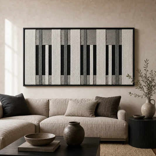 Large framed Monochrome Tempo hand-woven wall art hanging elegantly above a cozy beige sofa in a modern, neutral-toned living room setting.