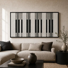Large framed Monochrome Tempo hand-woven wall art hanging elegantly above a cozy beige sofa in a modern, neutral-toned living room setting.