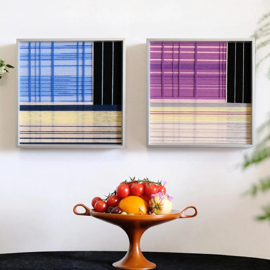 Night River Lantern hand-woven wool yarn wall art diptych featuring a left panel of ocean-blue and teal vertical stripes and a right panel of lavender and indigo stripes, framed in dark wood and displayed above a wooden console table.

