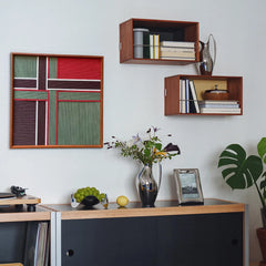 The textured fiber art piece displayed near wooden wall shelves with books, perfect for adding a sophisticated touch to a home office or study.