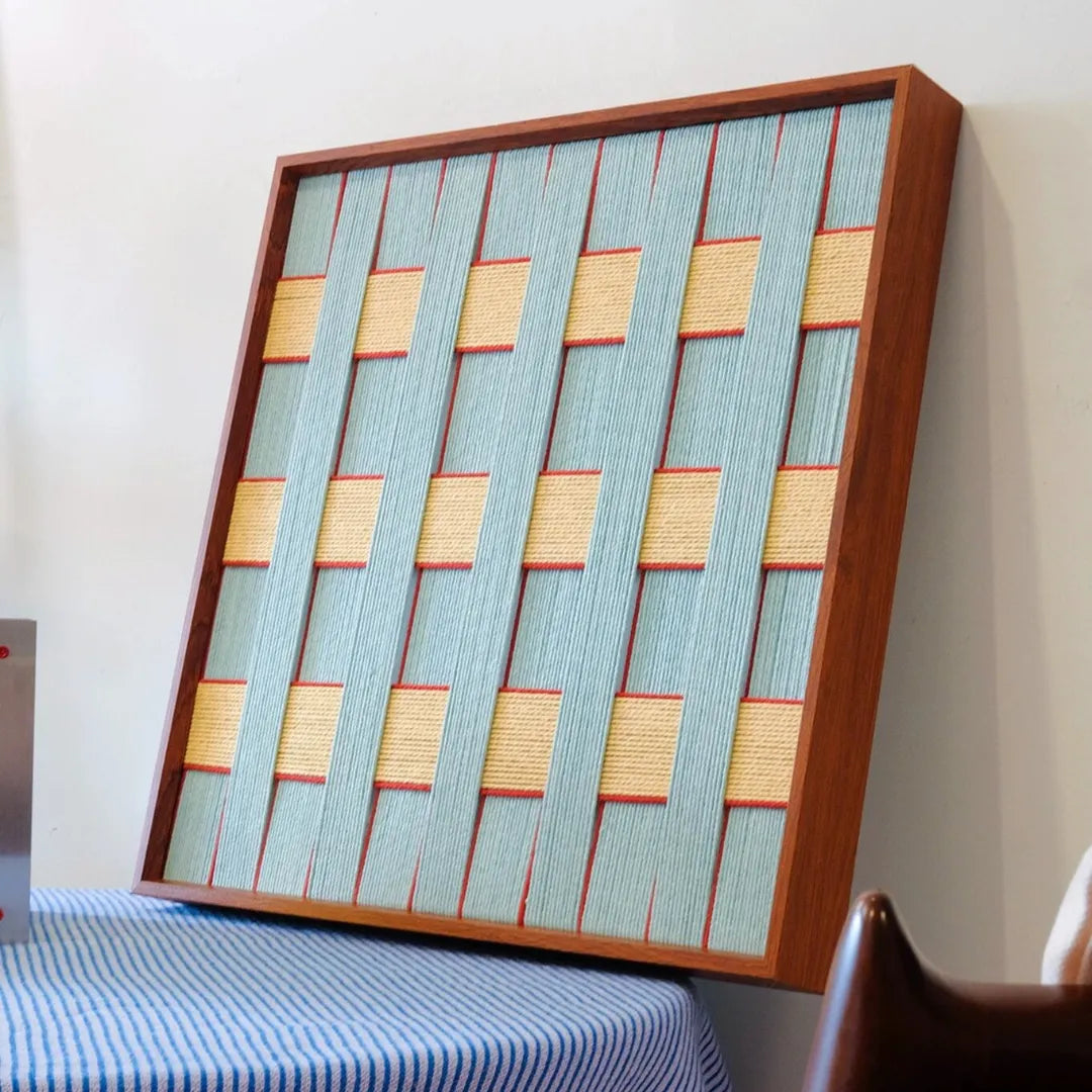 Diagonal view of the square yarn woven wall art showing its precise geometric weave of soft blue and pale yellow yarn with crisp edges
