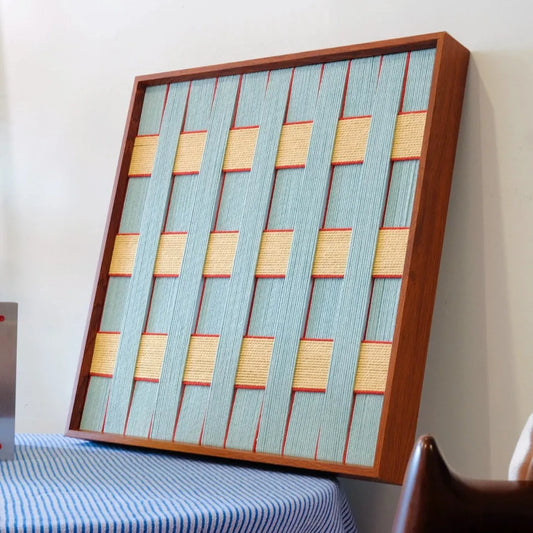 Diagonal view of the square yarn woven wall art showing its precise geometric weave of soft blue and pale yellow yarn with crisp edges
