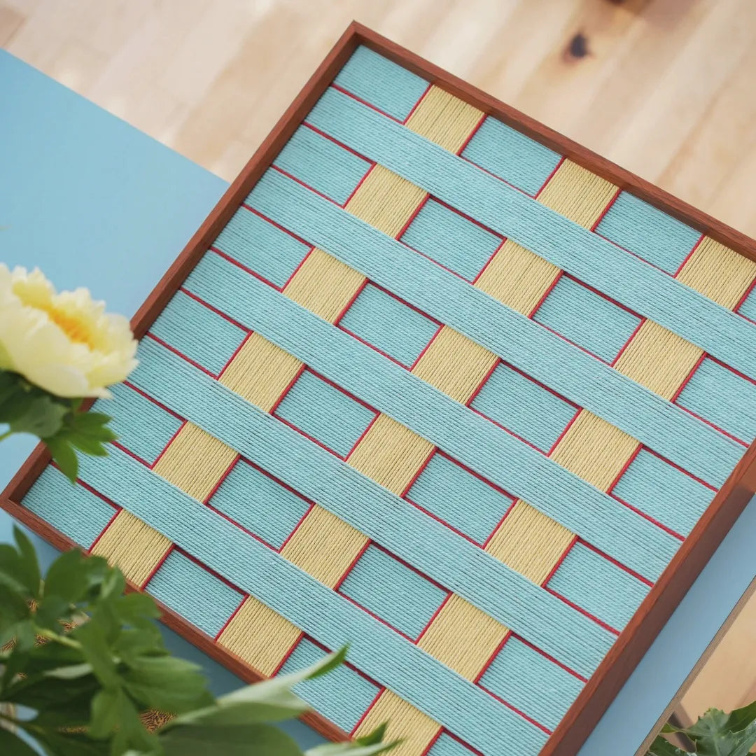 Overhead shot focusing on the symmetrical grid layout of the woven yarn art with equal-sized blue and yellow blocks
