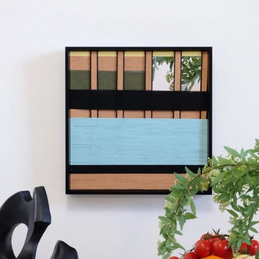 Outside The Window hand-woven yarn wall art featuring earth-tone vertical stripes above a soft sky-blue lower panel, framed in black wood.
