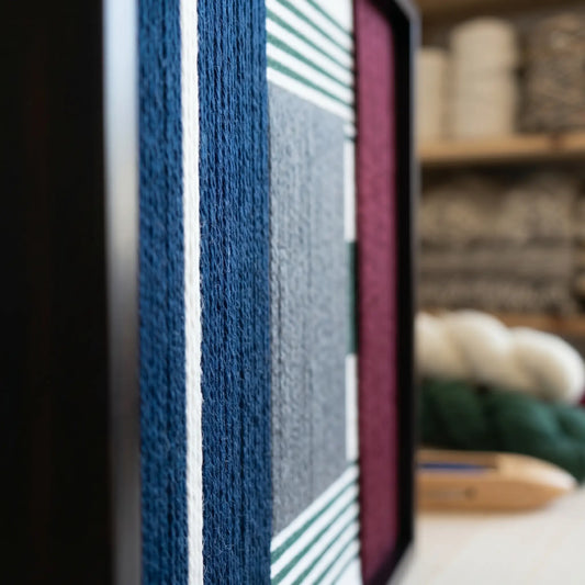 Macro side view of the fiber art highlighting the three-dimensional depth of the hand-wrapped navy and grey wool yarn.