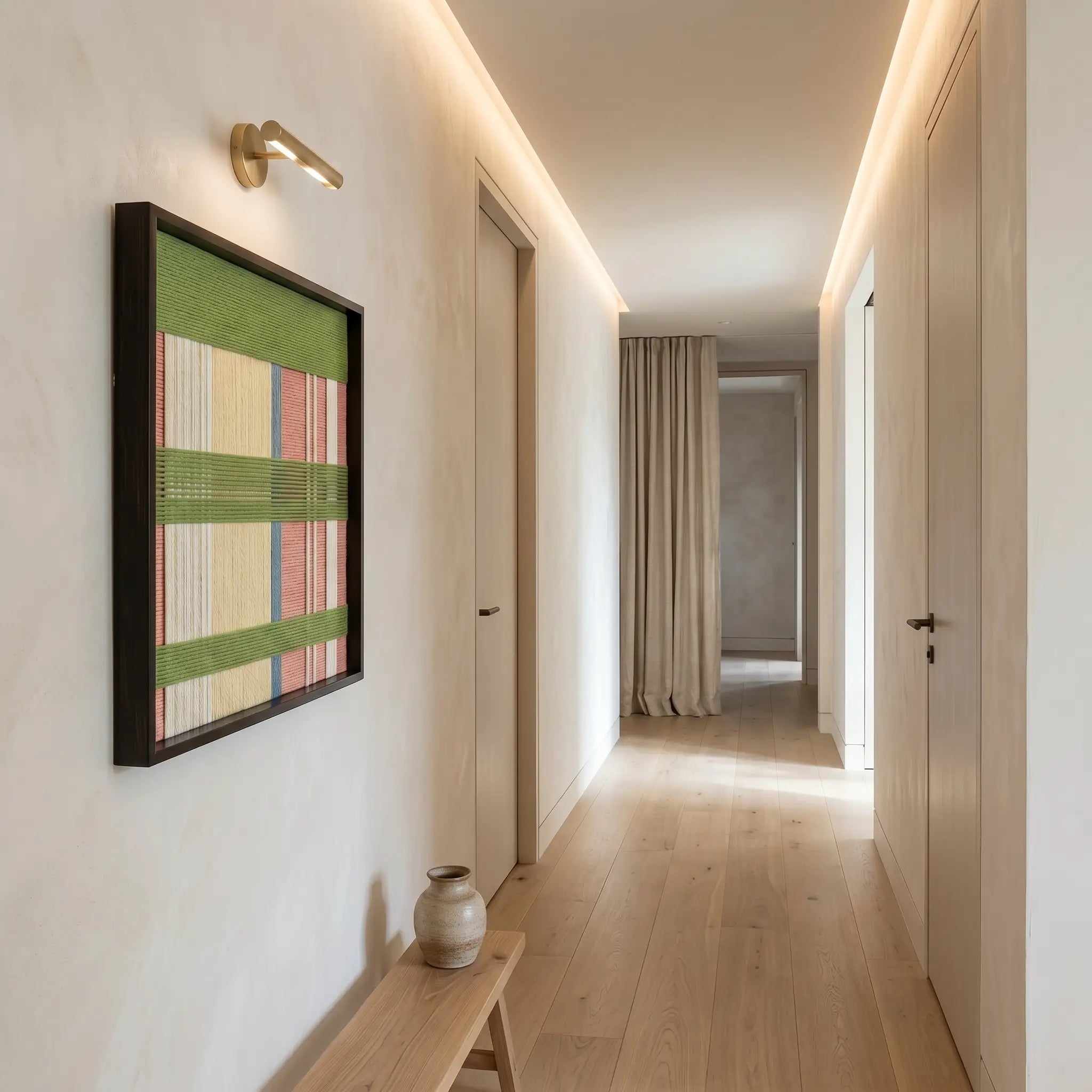 Pastel colored textured fiber art hanging in a bright modern hallway above a minimalist wooden bench.