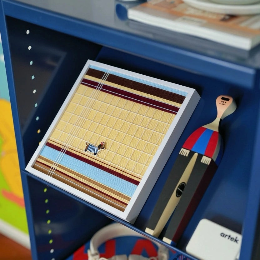Close-up of a smaller framed hand-woven wool tapestry featuring a dog character, styled on a modern blue industrial shelving unit.