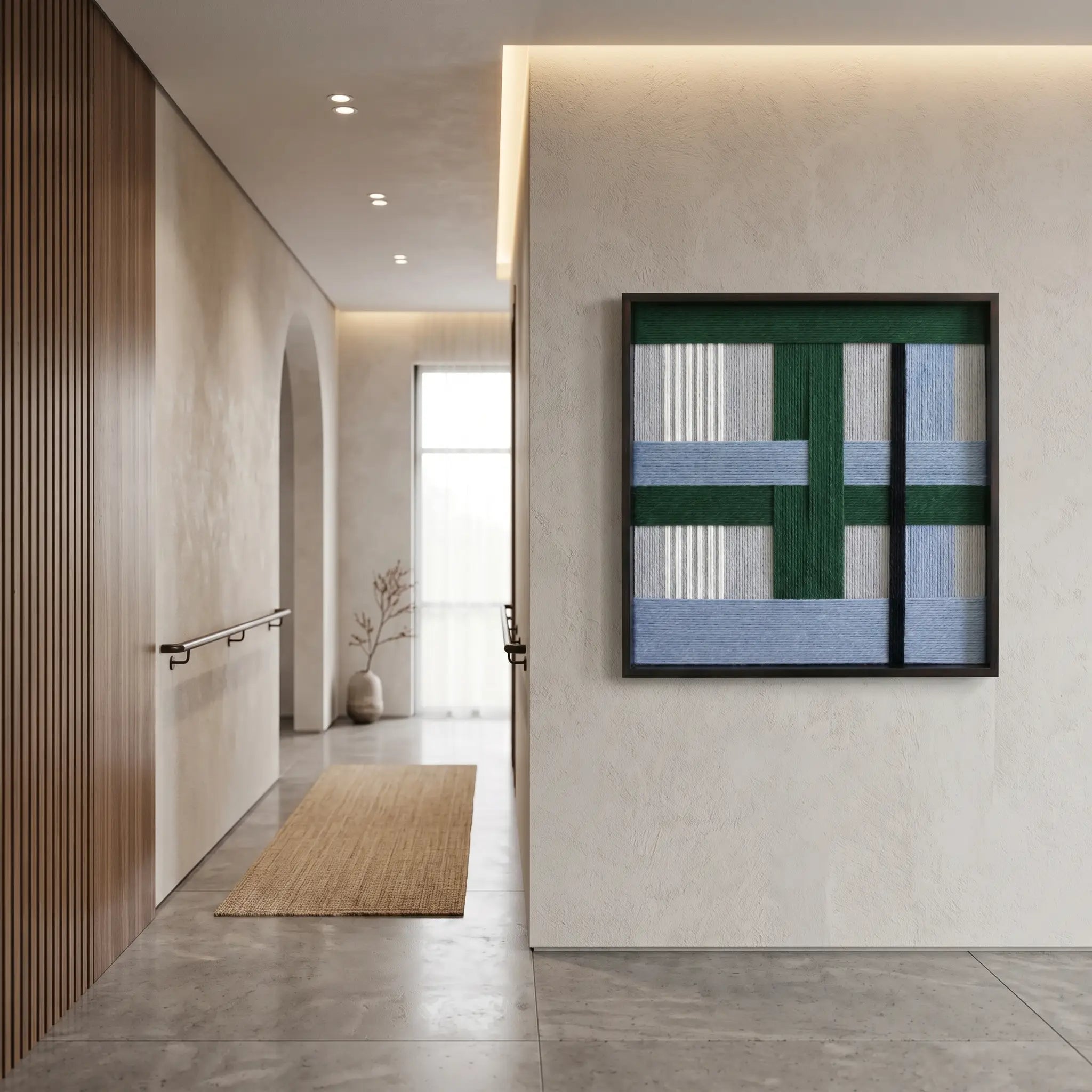 Vertical view of the green and blue textured fiber art hanging as a focal point in a minimalist modern hallway with a jute runner.