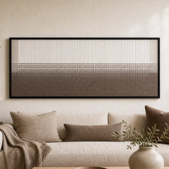 Large framed Quiet Thread hand-woven wall art hanging elegantly above a cozy cream sofa in a neutral living room.